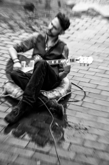 Junger Mann spielt sitzend im Regen Gitarre